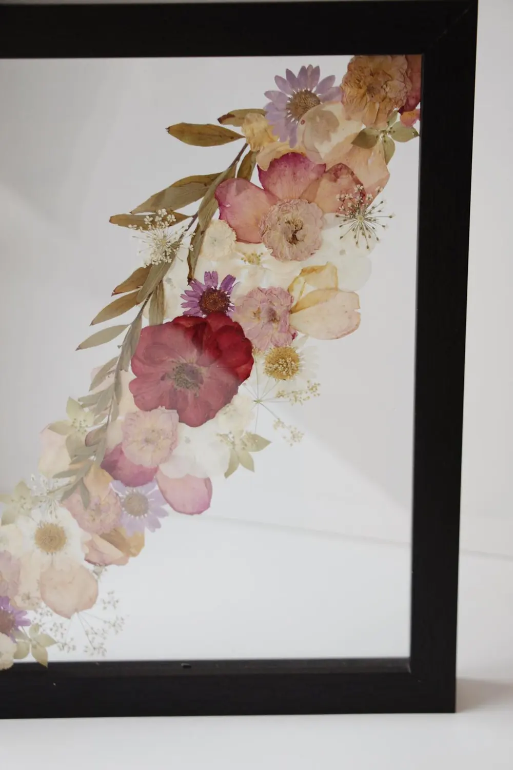 Black frame with a diagonal pressed garland of roses, daisies and eucalyptus