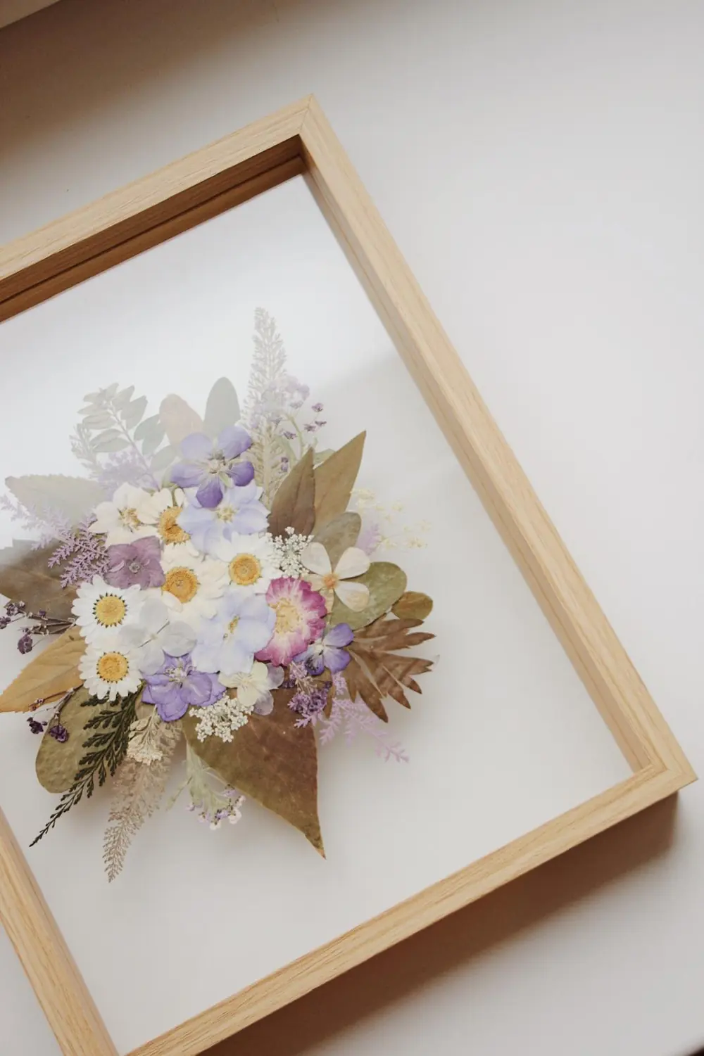 Light ash frame with a soft lilac and white pressed bouquet on clear glass