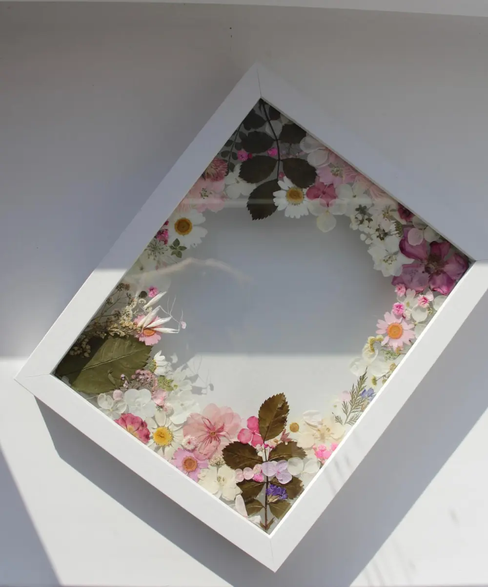 White box frame with a pressed flower wreath encircling clear glass