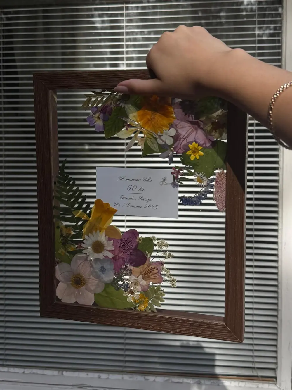 Dark wood double-glass frame with a pressed bouquet framing a handwritten anniversary card